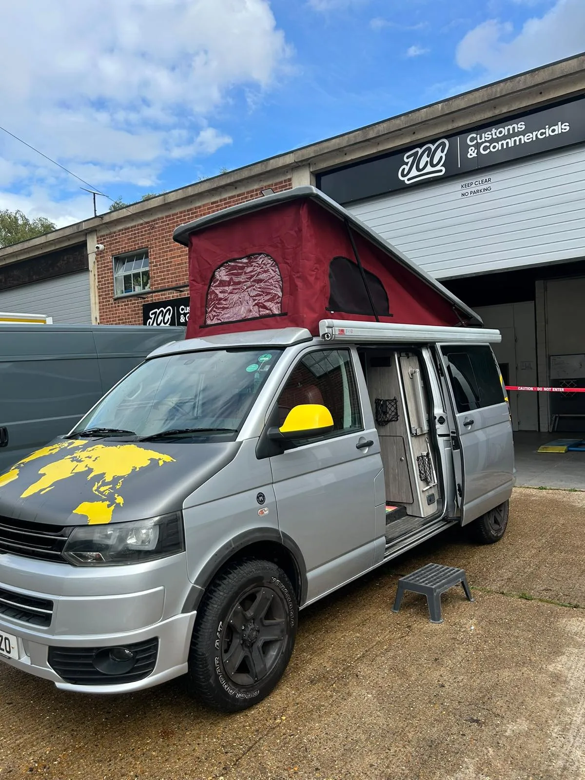 Campervan with its red fabric pop-top raised outside JCC
